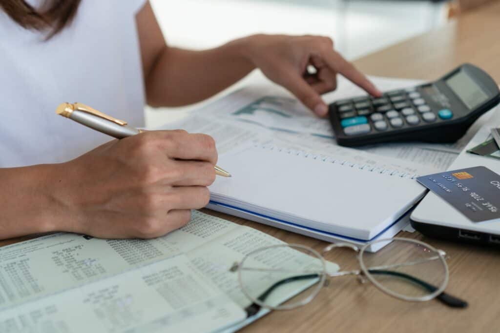 A person using a calculator with financial documents, a credit card, and glasses on the table, representing budgeting and financial planning.