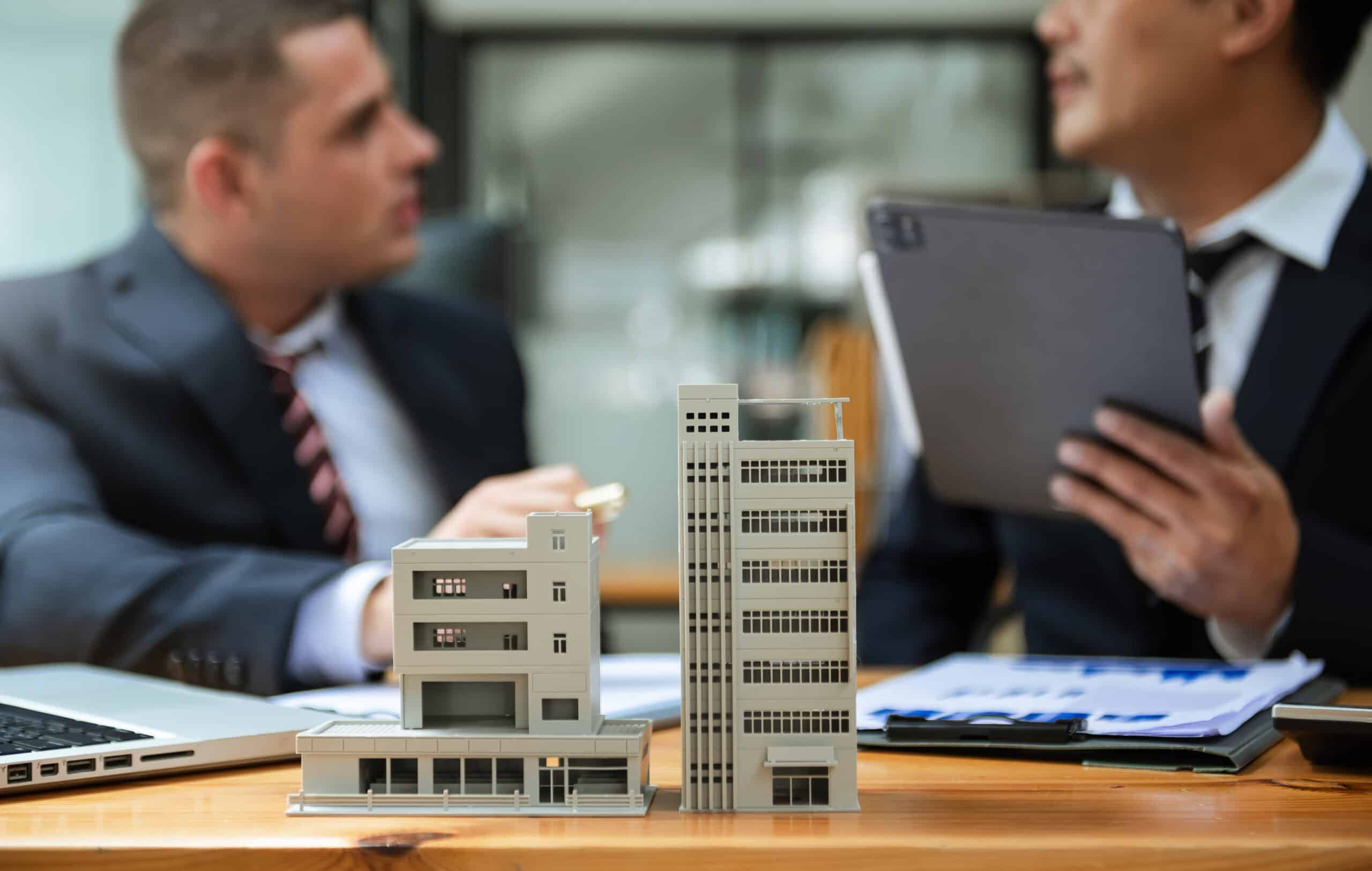 Two business professionals discuss commercial real estate investments, with small-scale condo representing property developments with condo mortgage requirements