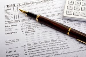 A close-up of a 1040 tax form with a gold fountain pen and calculator, symbolizing tax preparation and deductions.