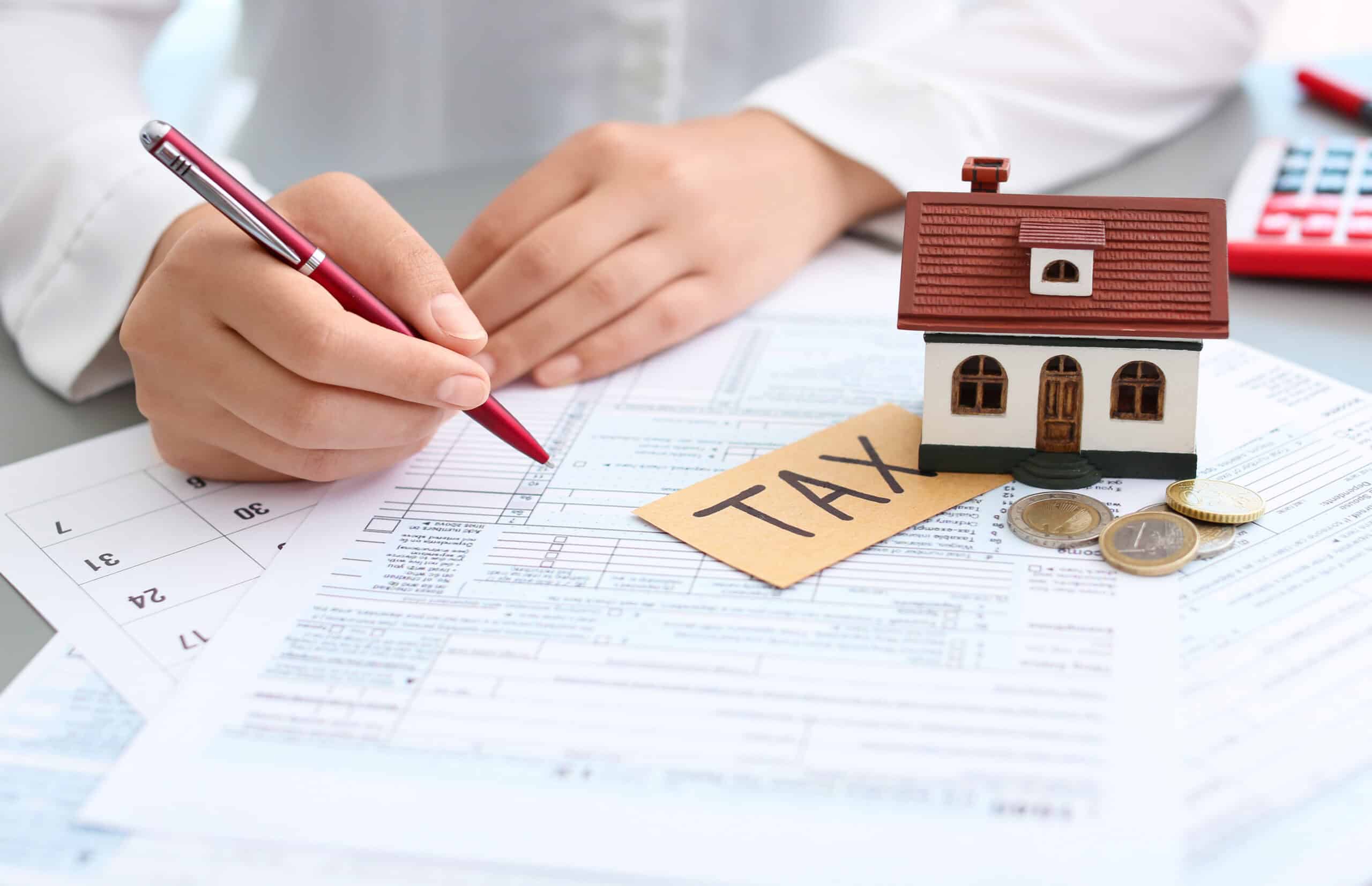 A person filling out tax documents with a small house model labeled 