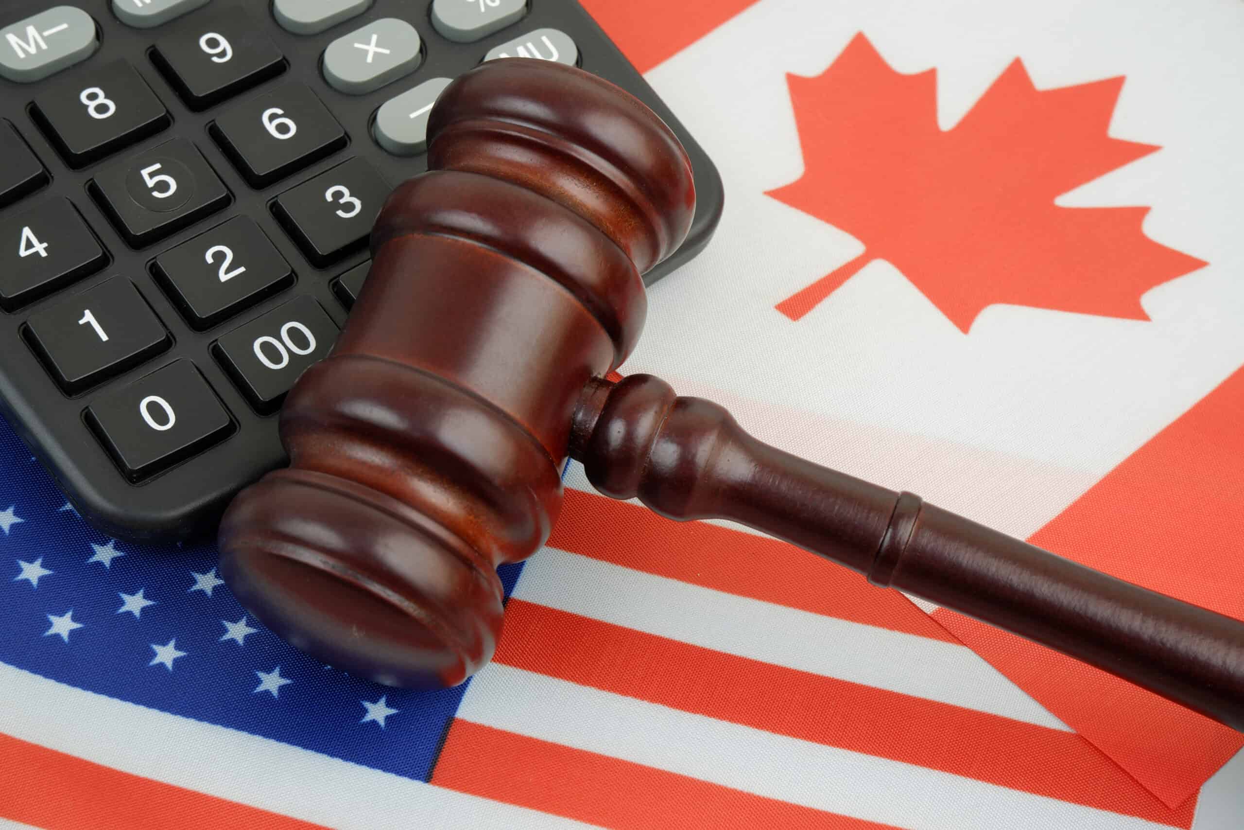 A wooden gavel and calculator placed over the U.S. and Canadian flags, symbolizing cross-border real estate laws and financial considerations.