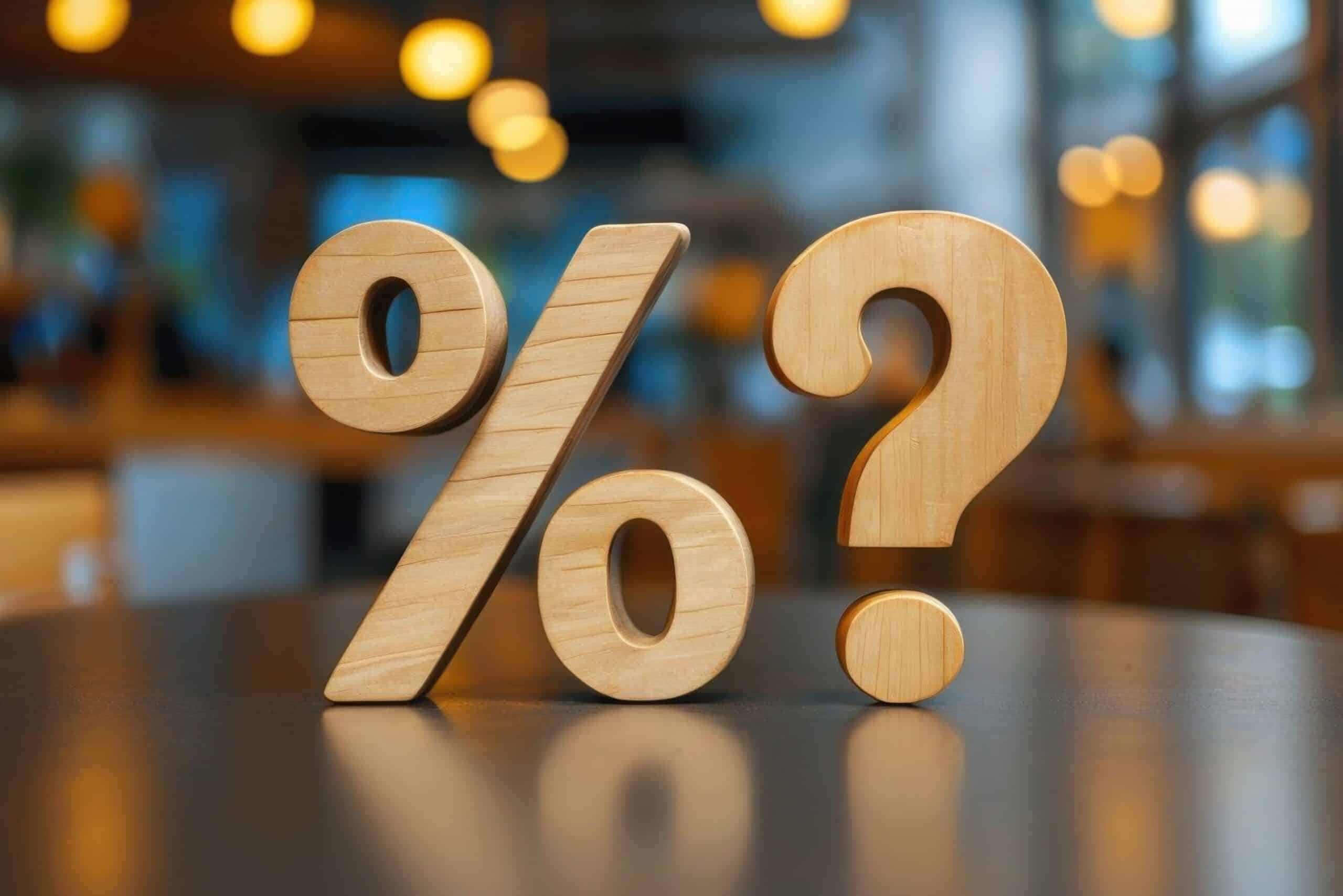 A wooden percentage symbol and a question mark on a table, representing mortgage interest rate uncertainty, with a blurred café-style background.