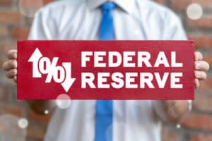 A person in business attire holding a red sign with “Federal Reserve” and interest rate symbols, representing the Fed’s influence on mortgage rates and lending.