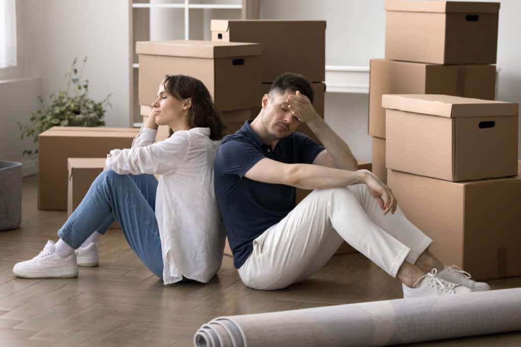 Divorcing couple sitting on floor surrounded by moving boxes, reflecting stress over homeownership and mortgage decisions.