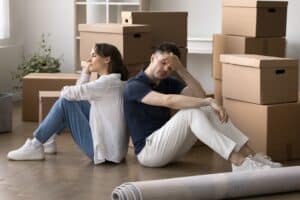 Divorcing couple sitting on floor surrounded by moving boxes, reflecting stress over homeownership and mortgage decisions.
